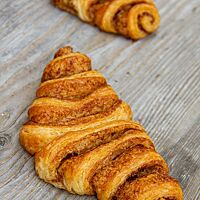 Auf einem rustikalen Holztisch liegen zwei goldbraun ausgebackene, saftige Franzbrötchen.