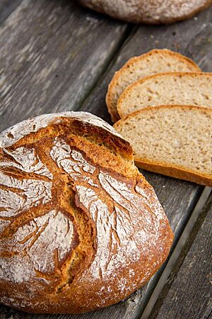Das kräftig ausgebackene, rustikal aufgerissene Pane Rustico aus festem Teig liegt angeschnitten auf einem Tisch.