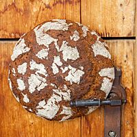 Ein runder Roggenbrot-Laib klemmt zwischen Türblatt und Klinke einer Holztür.