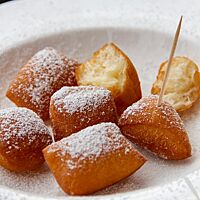 Auf einem Teller liegen mehrere goldbraun ausgebackene, mit Puderzucker bestreute Stücke Schmalzgebäck.