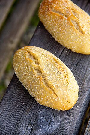 Goldgelb ausgebackene, rustikal aufgerissene Maisbrötchen liegen auf einer Holzlatte.