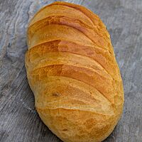 Ein goldgelb ausgebackenes, längliches Weißbrot mit gefensterter Kruste liegt auf einem rustikalen Holztisch.