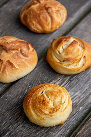 Vier Splitterbrötchen mit goldbrauner Kruste liegen auf einer rustikalen Holzbank.