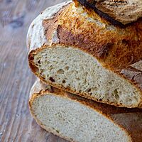 Zwei übereinanderliegende Brotlaibe zeigen den Vergleich zwischen langer und kurzer Stockgare. Das oben liegende Brot mit langer Stockgare hat eine Krume mit kleiner, unregelmäßiger Porung. Das unten liegende Brot mit kurzer Stockgare hat eine feine und gleichmäßige Porung.