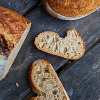 Ein angeschnittener Laib und zwei Scheiben zeigen die rustikale Kruste und mittlere Porung des Sonnensternbrotes.