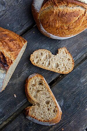 Ein angeschnittener Laib und zwei Scheiben zeigen die rustikale Kruste und mittlere Porung des Sonnensternbrotes.