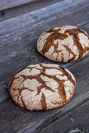 Zwei rustikal aufgerissene Brotlaibe mit leicht bemehlter Kruste liegen auf einer rustikalen Holzbank.