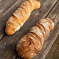 Zwei kräftig ausgebackene Wurzelbrote mit Walnüssen (rechts) und ohne Walnüsse (links) liegen auf einem rustikalen Holztisch.