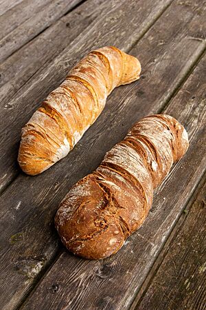 Zwei kräftig ausgebackene Wurzelbrote mit Walnüssen (rechts) und ohne Walnüsse (links) liegen auf einem rustikalen Holztisch.