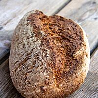 Ein kräftig ausgebackener Brotlaib liegt auf einem rustikalen Holztisch.