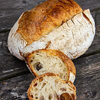 Zwei Scheiben mit grobporiger Krume liegen angelehnt an den Brotlaib mit knuspriger, krosser Kruste.
