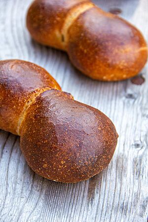 Zwei paarweise aneinandergebackene Weizenbrötchen liegen dunkelbraun ausgebacken auf einem Holztisch.