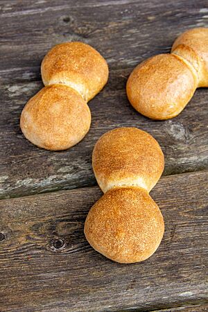 Drei goldgelb ausgebackene Oberalbener Doppelwecken mit glatter Oberfläche liegen auf einem rustikalen Holztisch.