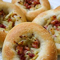 Die goldgelb ausgebackenen Brötchen sind in der Mitte mit gedünstetem Bauchspeck, Zwiebeln und Knoblauch belegt und haben einen breiten Rand.