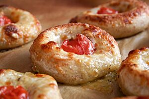 Fünf ausgebackene Kartoffel-Pizza-Nester, belegt mit Mozzarella und einer kleinen Tomate, liegen auf Backpapier.