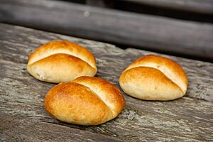 Drei Großauheimer Milchbrötchen mit mittig eingedrückter Kruste liegen auf einem rustikalen Holztisch.