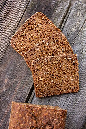 Im angeschnittenen Schwarzbrot sind jede Menge Saaten, grober Roggenschrot und Buchweizenkörner in der dunkelbraunen Krume zu sehen.