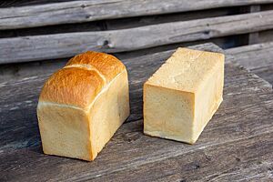 Zwei sehr hell ausgebackene Kastenbrote liegen auf einem rustikalen Holztisch – eines mit gewölbter, das andere mit gerader Oberseite.