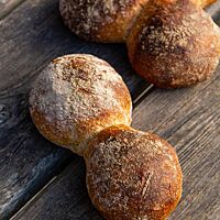 Die kräftig ausgebackenen Bürli in Form von Doppelbrötchen liegen auf einem rustikalen Holztisch.