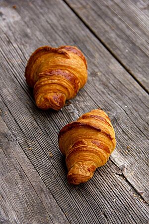 Zwei goldgelb ausgebackene Dinkelcroissants mit glänzender Oberfläche liegen auf einem rustikalen Holztisch.