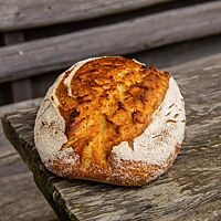 Das kräftig ausgebackene, rustikal aufgerissene Kamutbrot mit bemehlter Kruste liegt auf einem Holztisch.
