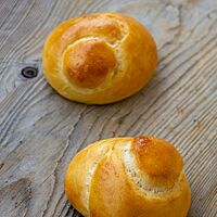 Zwei goldgelb ausgebackene Schweizer Knoten mit glänzender Oberfläche liegen auf einem rustikalen Holztisch.