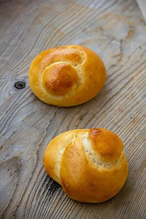 Zwei goldgelb ausgebackene Schweizer Knoten mit glänzender Oberfläche liegen auf einem rustikalen Holztisch.