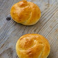 Zwei goldgelb ausgebackene Schweizer Knoten mit glänzender Oberfläche liegen auf einem rustikalen Holztisch.
