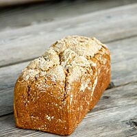 Ein in der Kastenform gebackenes Vollkornbrot liegt auf einem rustikalen Holztisch.