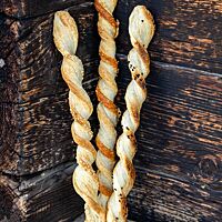 Die knusprig ausgebackenen, verdrehten Blätterteigstangen lehnen an einer Holzwand.