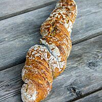 Die goldbraun ausgebackene Leinwurzel mit leicht bemehlter Kruste liegt auf einem rustikalen Holztisch.