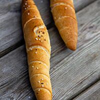 Zwei hell ausgebackene, mit grobem Salz und Kümmel bestreute Stangerl liegen auf einem Tisch.