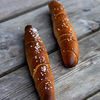 Zwei dunkel ausgebackene, mit grobem Salz bestreute Almstangerl liegen auf einem rustikalen Holztisch.