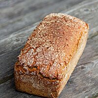 Das kastenförmige Jasminreisbrot mit glatter Oberfläche liegt auf einem rustikalen Holztisch.