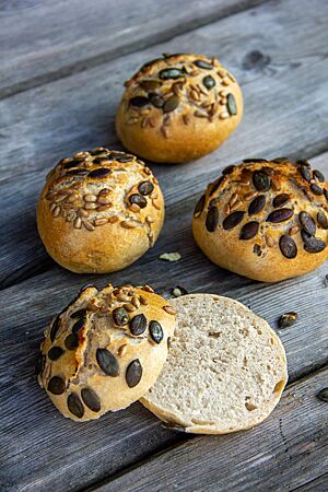 Ein halbiertes Brötchen zeigt die feinporige, lockere Krume und die dünne, goldgelb ausgebackene Kruste mit rustikalem Ausbund und Saatenaufstreu.
