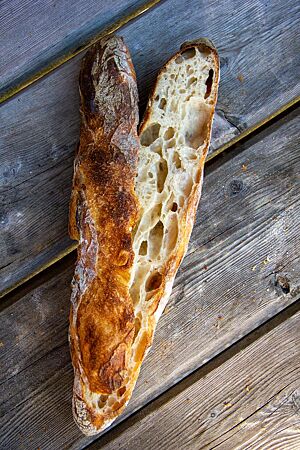 Ein aufgeschnittenes Baguette zeigt die kräftig ausgebackene Kruste sowie die grobporige, lockere und saftige Krume.