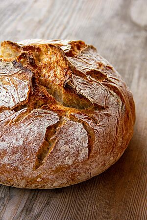 Ein rustikal aufgerissenes, kräftig ausgebackenes Weizensauerteigbrot mit krosser Kruste liegt auf einem Holztisch.