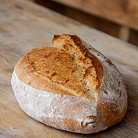 Das rustikale, weit aufgerissene Ruchbrot liegt auf einem Holztisch.