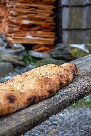 Auf einem rustikalen, verwitterten Holzbrett liegt ein längliches Fladenbrot aus Ruchmehl.