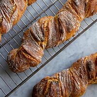 Drei verdrehte Dinkel-Emmer-Wurzeln mit leicht bemehlter, knuspriger Kruste liegen auf einem Gitterrost.