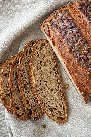 Vier Scheiben Kürbiskernbrot zeigen die leicht grünliche Krume und ungleichmäßige Porung.