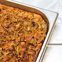 Die goldbraun ausgebackene Roggenfocaccia liegt in einem tiefen Blech und ist mit karamellisierten Zwiebeln belegt.