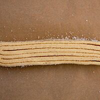 Ein ungebackenes Schweinsohr liegt auf einem Stück Backpapier.