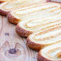 Eine Reihe angeschoben gebackener Schweinsohren liegt auf einem hellen Holztisch.