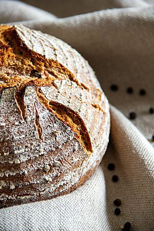 In einem Leinentuch liegen einige ganze Pfefferkörner und das kräftig ausgebackene Pfefferbrot.