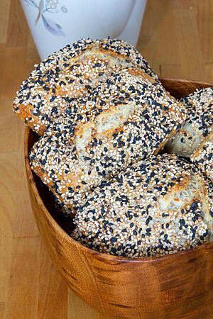 Die goldgelb ausgebackenen Mischbrötchen mit schwarzem und hellem Sesam auf der Oberfläche liegen in einer Holzschale.