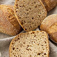 Ein aufgeschnittenes Brötchen lässt die klein- bis mittelporige Krume erkennen, die sich farblich kaum von der braunen Kruste unterscheidet.