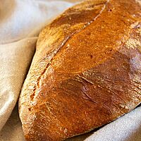 Ein kräftig ausgebackenes, an den Enden spitz zulaufendes Weizenbrot liegt auf einem Leinentuch.