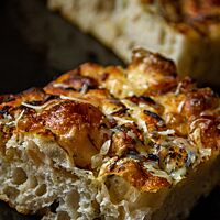 Ein Stück Focaccia mit heller, lockerer Krume ist auf der goldbraunen Kruste mit Kräutern bestreut.