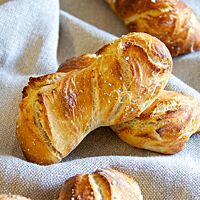 Mehrere Dinkelbrötchen mit hellen Salzkristallen auf der knusprigen Kruste liegen auf einem Leinentuch.